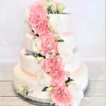 Efektowny tort z masy cukrowej ozdobiony żywymi kwiatami i ozdobną wstążką