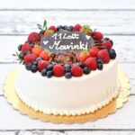 Tort urodzinowy wykończony śmietaną, udekorowany owocami sezonowymi i korą czekoladową
